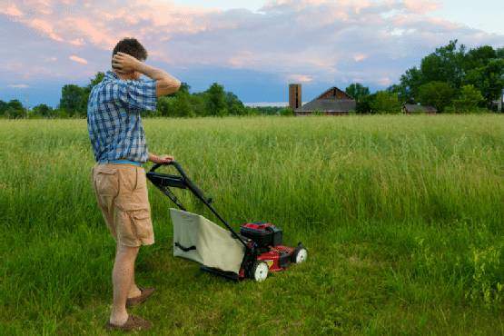 A person mowing long grass in a yard of a house