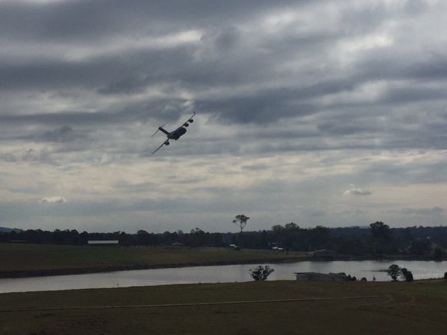 A large field with a small pond in the middle, and an airplane flying across.